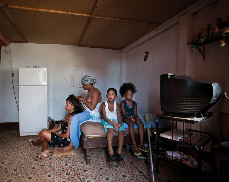 Odelin does her neighbour Kirenia hair while Nortis and  Marian watch television.- Sol Street, La Habana Vieja