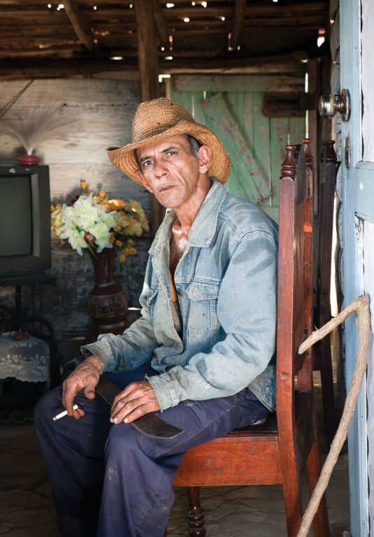 Miquel’s skin glistens from sweat as he sits down to enjoy a cigarette. He has just returned home from working in the fields where he has been cutting grass with a machete and wooden gancho which he uses as an aid in pull the grass that has been cut out of his way.